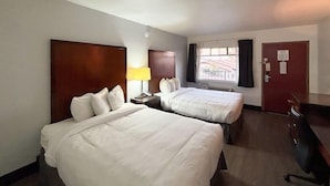 Hotellihuone, jossa on kaksi sänkyä, työpöytä, lamppu, ikkuna verhoilla ja ovi.