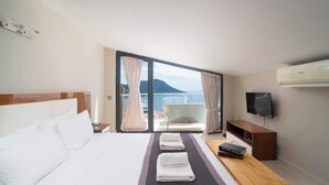 Een hotelkamer met een bed, een televisie, een houten nachtkastje, een balkon met een stoel en uitzicht op zee.