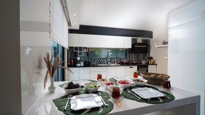 Een moderne keuken met witte kasten, een zwart-wit achterwand, en een eethoek met groene placemats, borden en bestek.