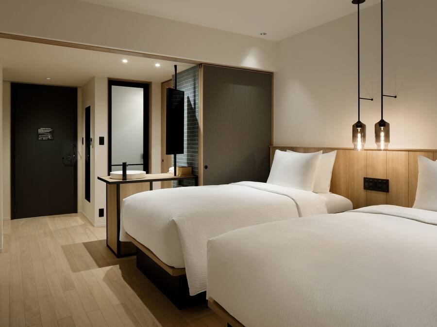 A hotel room with two beds, a wooden headboard, a bedside table, a mirror, and a hanging light fixture.