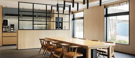 A modern kitchen with a long wooden table and chairs, built-in appliances, and large windows.