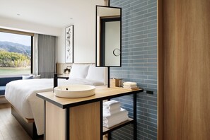 Ein modernes Hotelzimmer mit einem großen Bett, einem runden Waschbecken, einem Spiegel und Bergblick durch das Fenster.