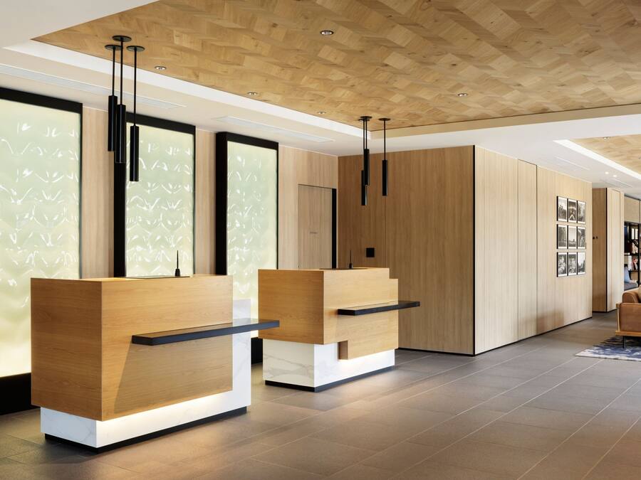 A modern reception area with wooden reception desks, a high ceiling with wooden panels, and a minimalist design.