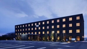 Ein modernes Hotelgebäude mit flacher Fassade, zahlreichen Fenstern und einem Parkplatz davor.
