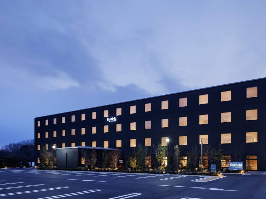 A modern hotel building with a flat facade, multiple windows, and a parking lot in front.