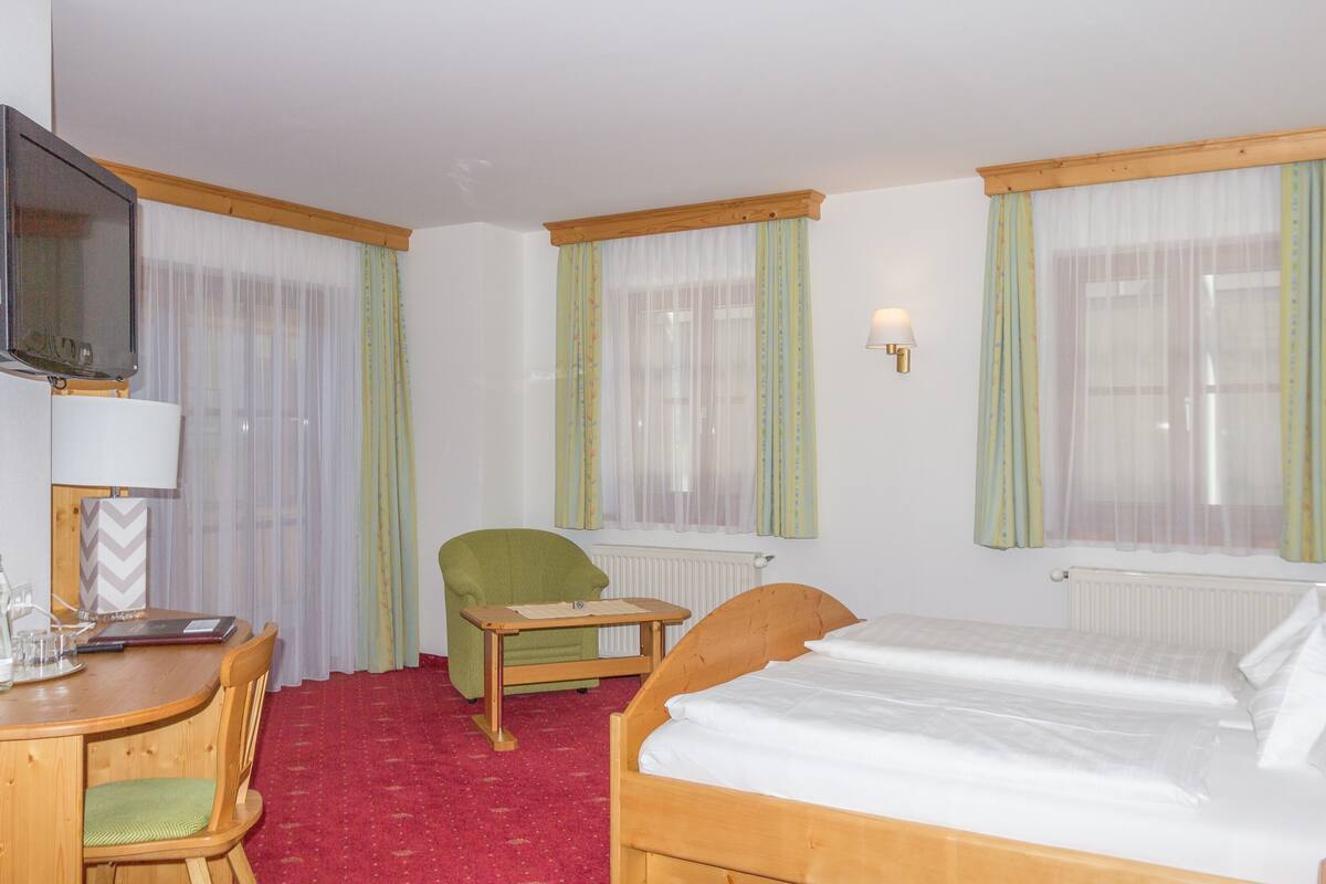 Une chambre d’hôtel avec un lit, un bureau et une chaise, une télévision et une fenêtre avec des rideaux.