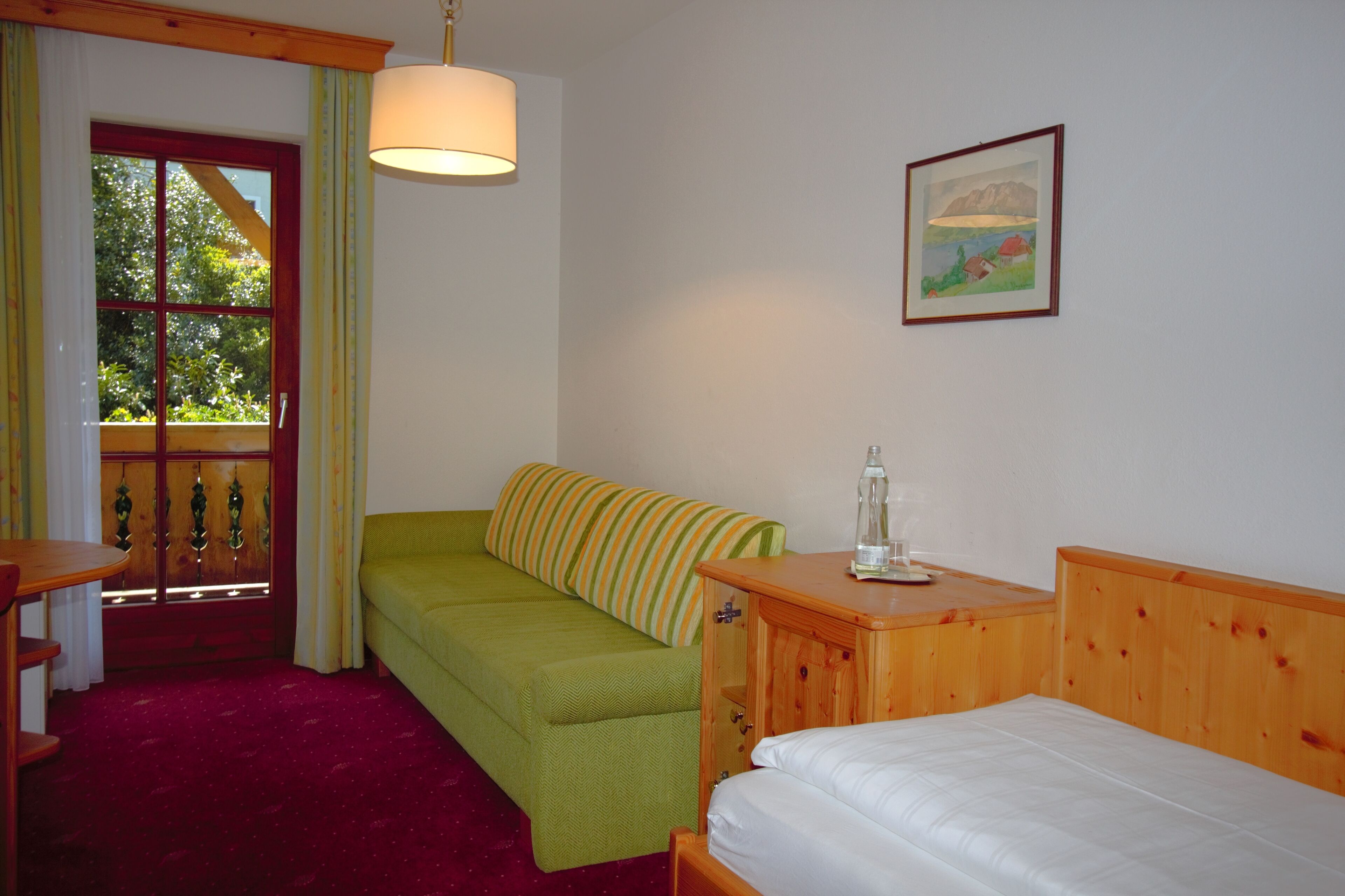 Una habitación con una cama de madera, un sofá verde, una mesita de noche de madera, una mesa y una ventana con cortinas.