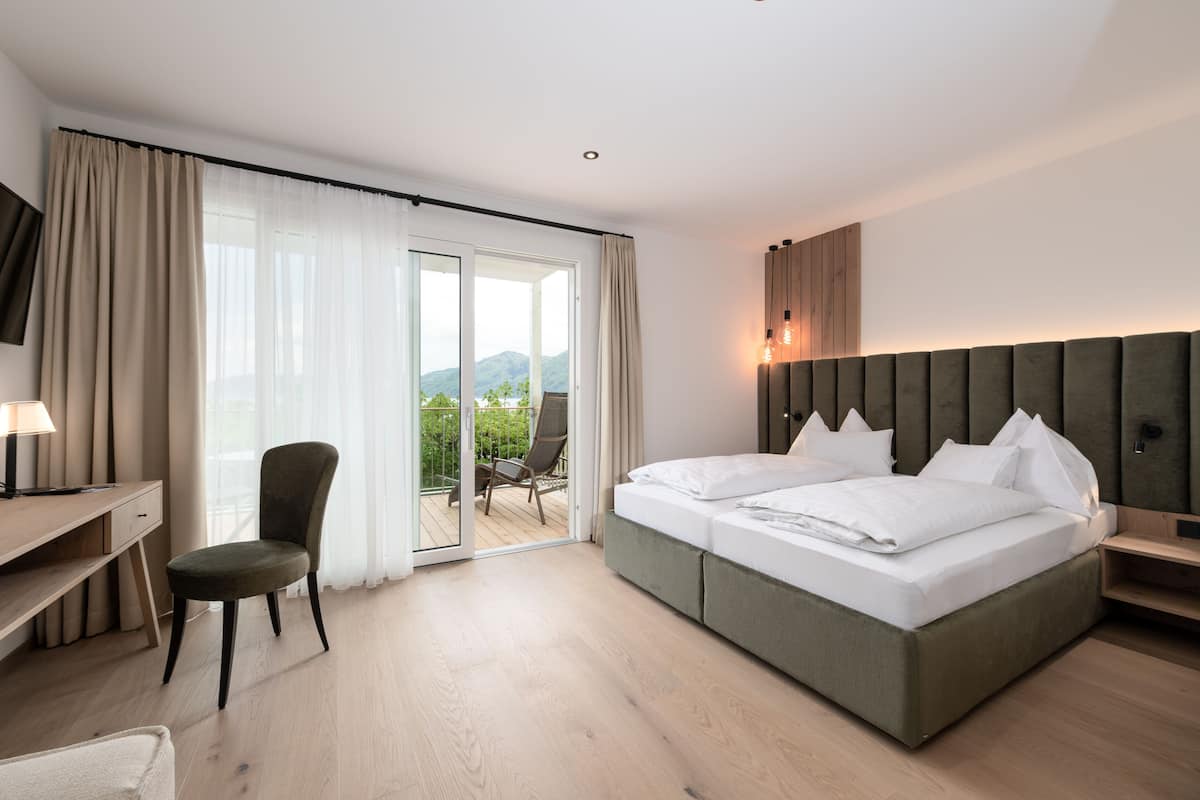 Une chambre d’hôtel moderne équipée d’un lit, d’un bureau, d’une chaise et d’un balcon offrant une vue sur les montagnes.
