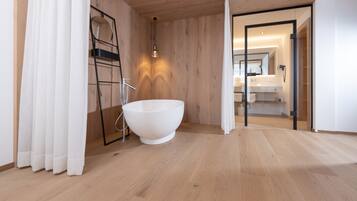 Un bagno moderno con una grande vasca da bagno bianca, pavimento in legno e cabina doccia in vetro.