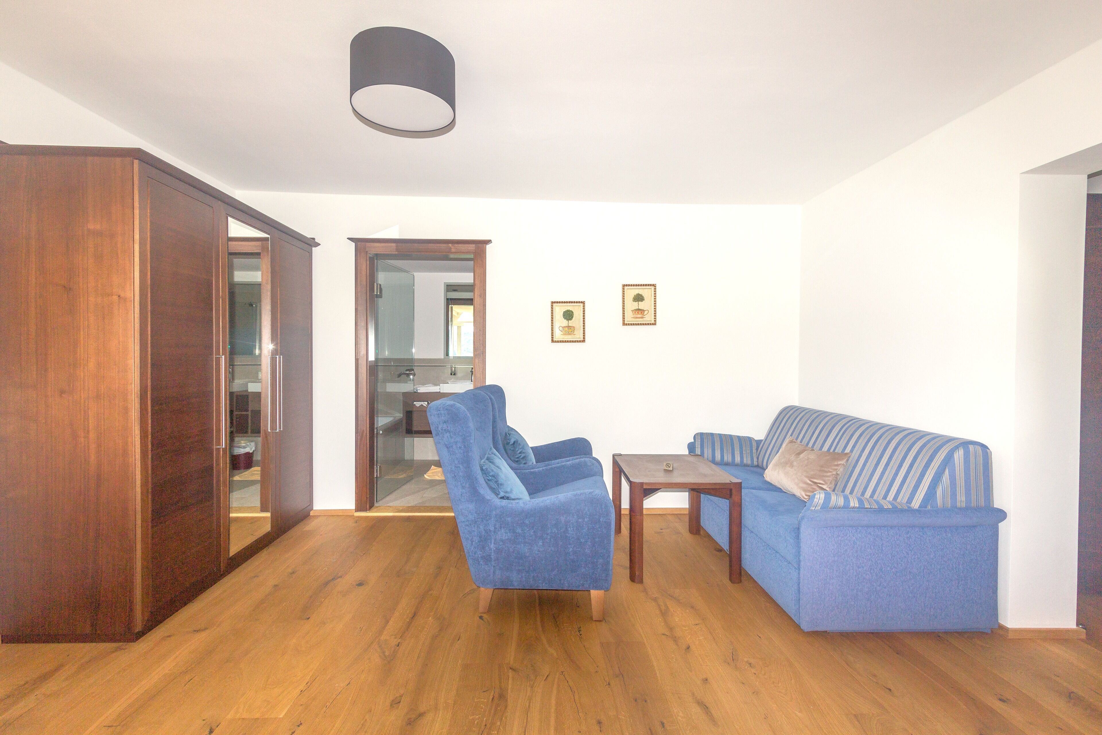 A living room with a blue armchair, a blue sofa, a wooden cabinet, and a small table.