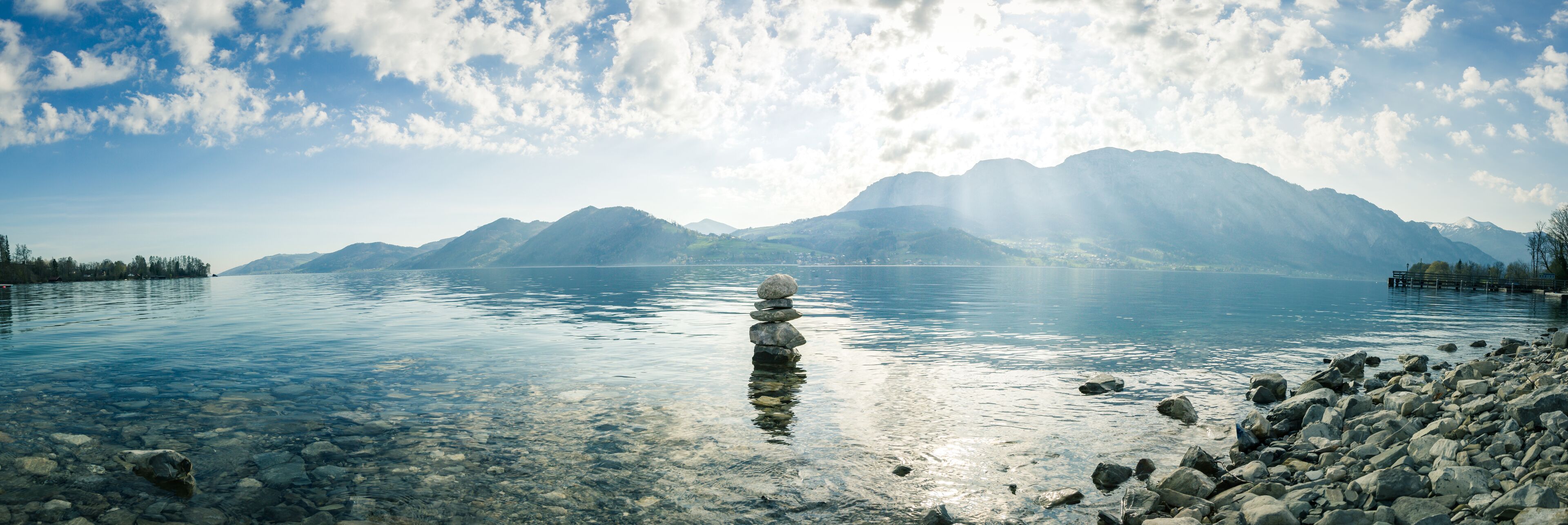 Un lago limpido con una roccia in primo piano e montagne sullo sfondo.