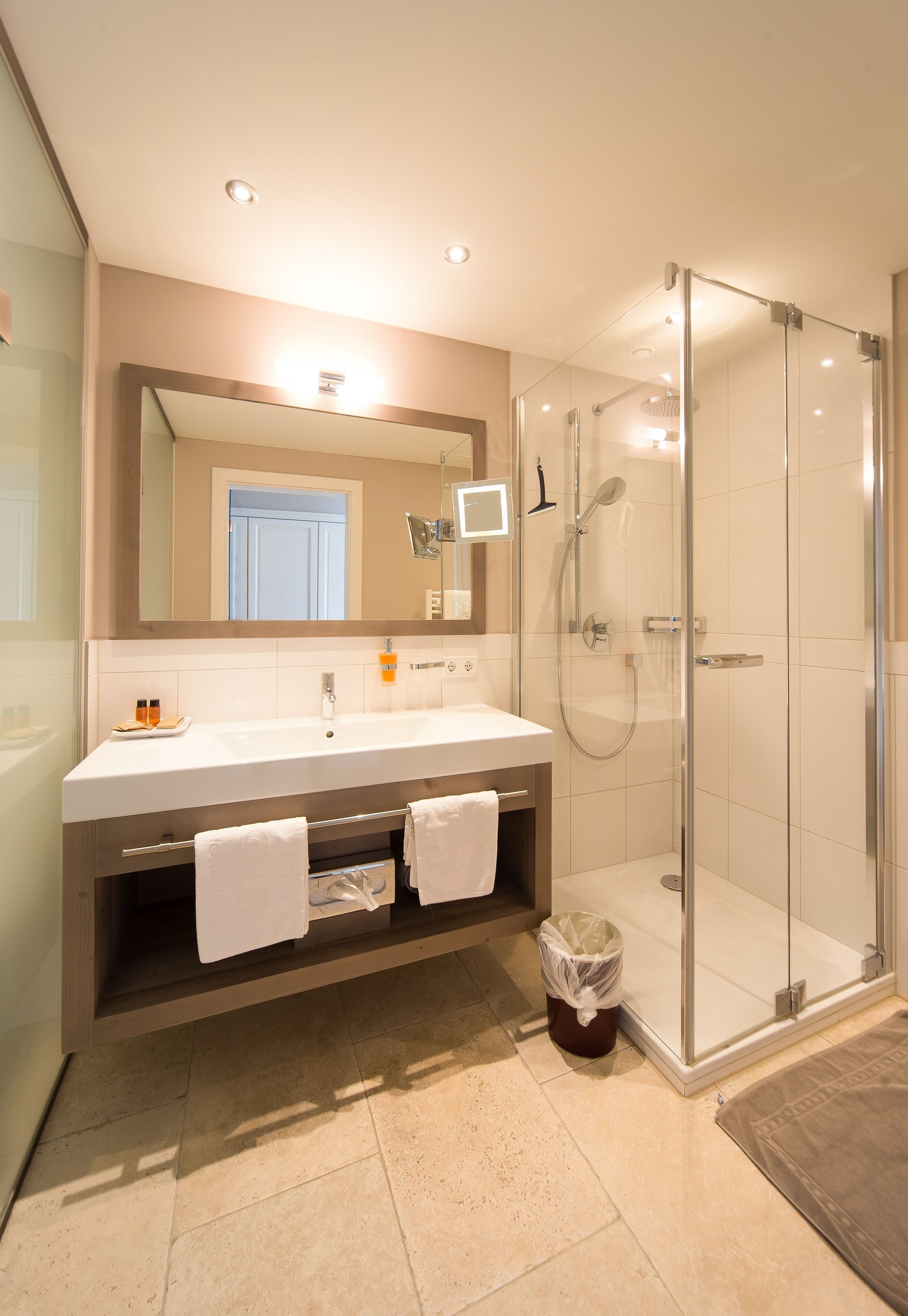 A modern bathroom with a glass-enclosed shower, a large mirror, and a vanity with a sink and towel rack.