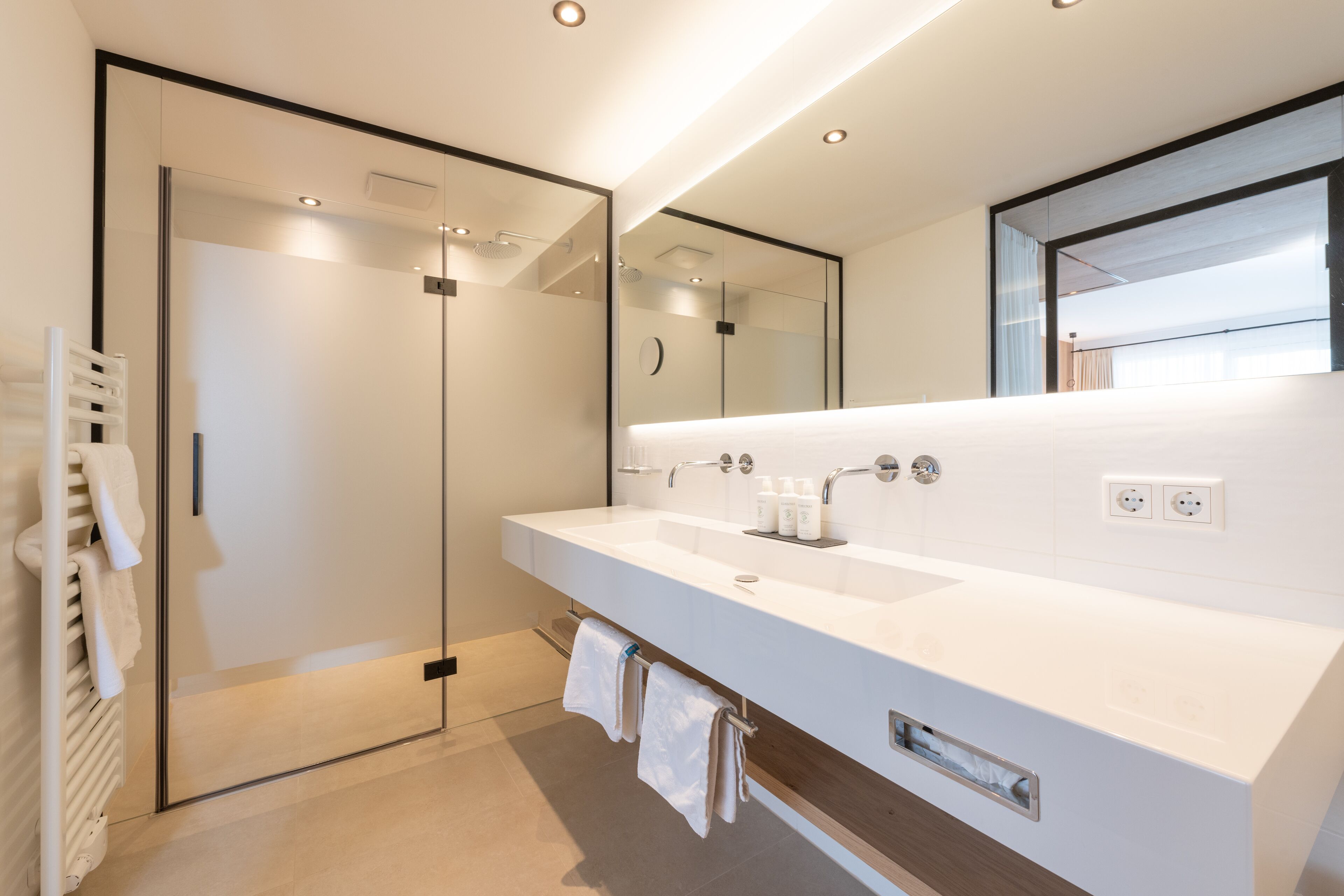 A modern bathroom with a large mirror, a white sink, and a glass shower enclosure.