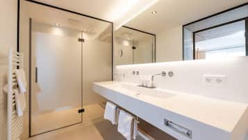 A modern bathroom with a large mirror, a white sink, and a glass shower enclosure.