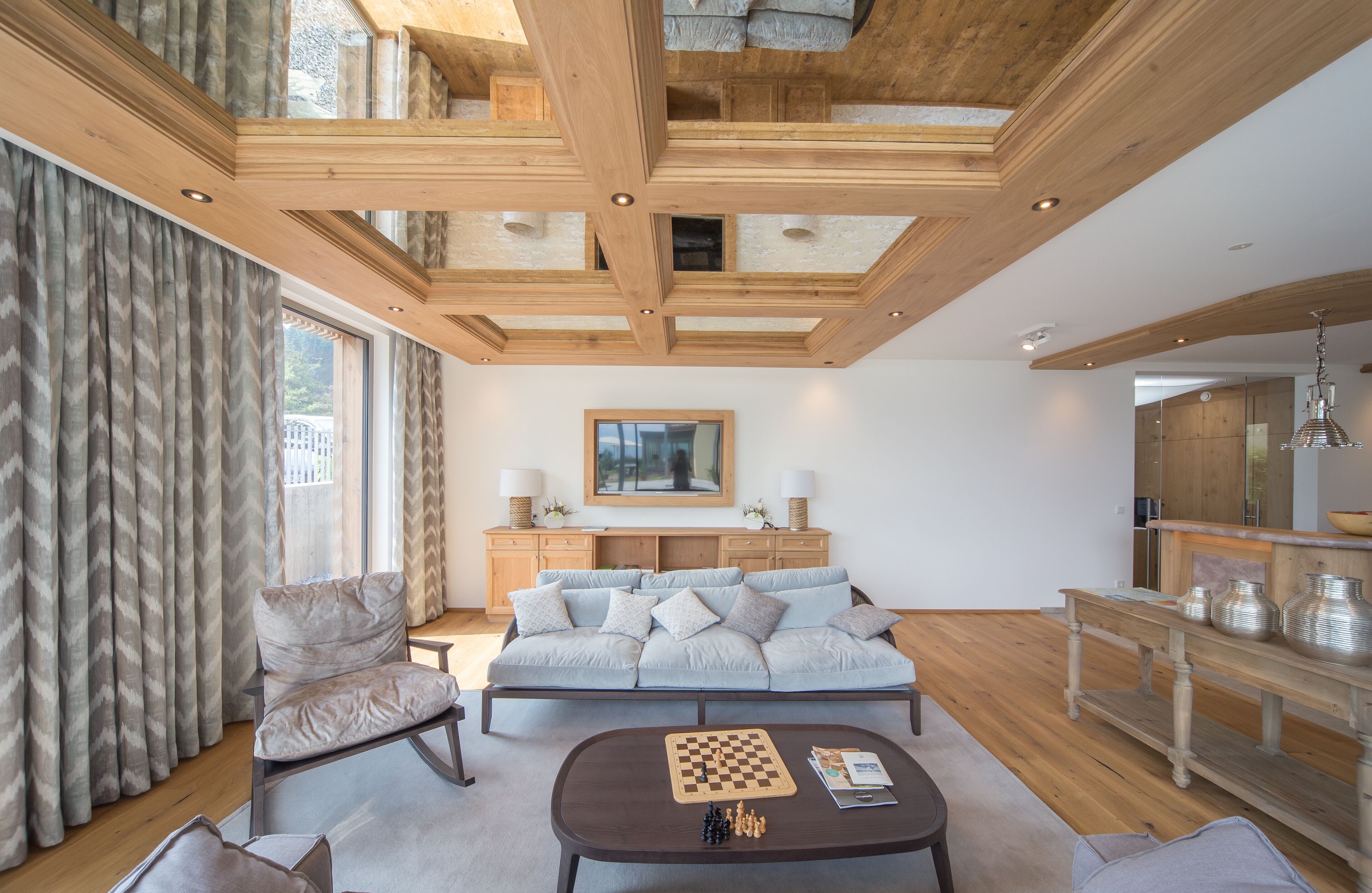 A modern living room with a wooden ceiling, a sofa, a coffee table with chess pieces, and a dining area with a wooden table and chairs.