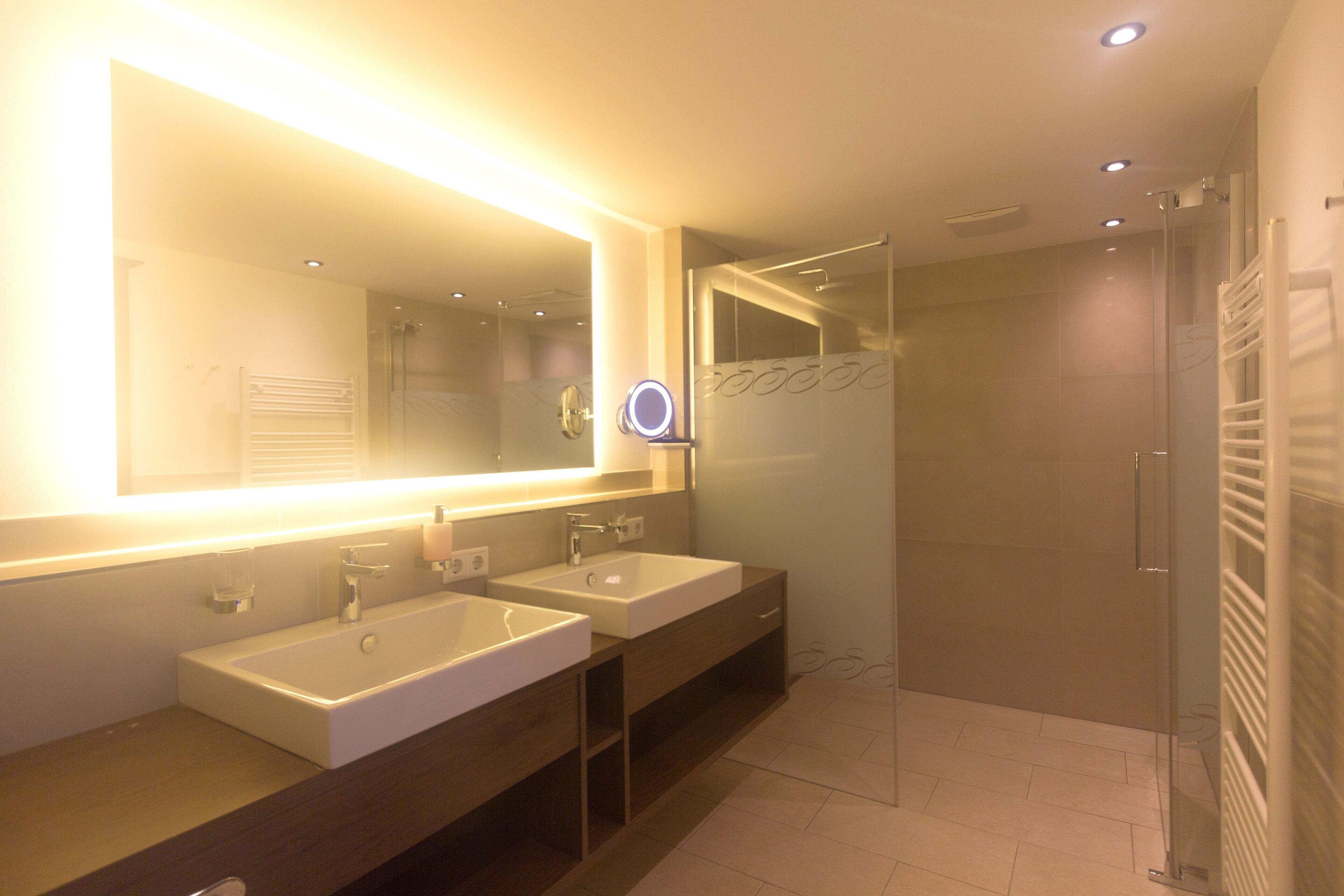 Un baño moderno con dos lavamanos, un espejo grande y cabina de ducha de vidrio.