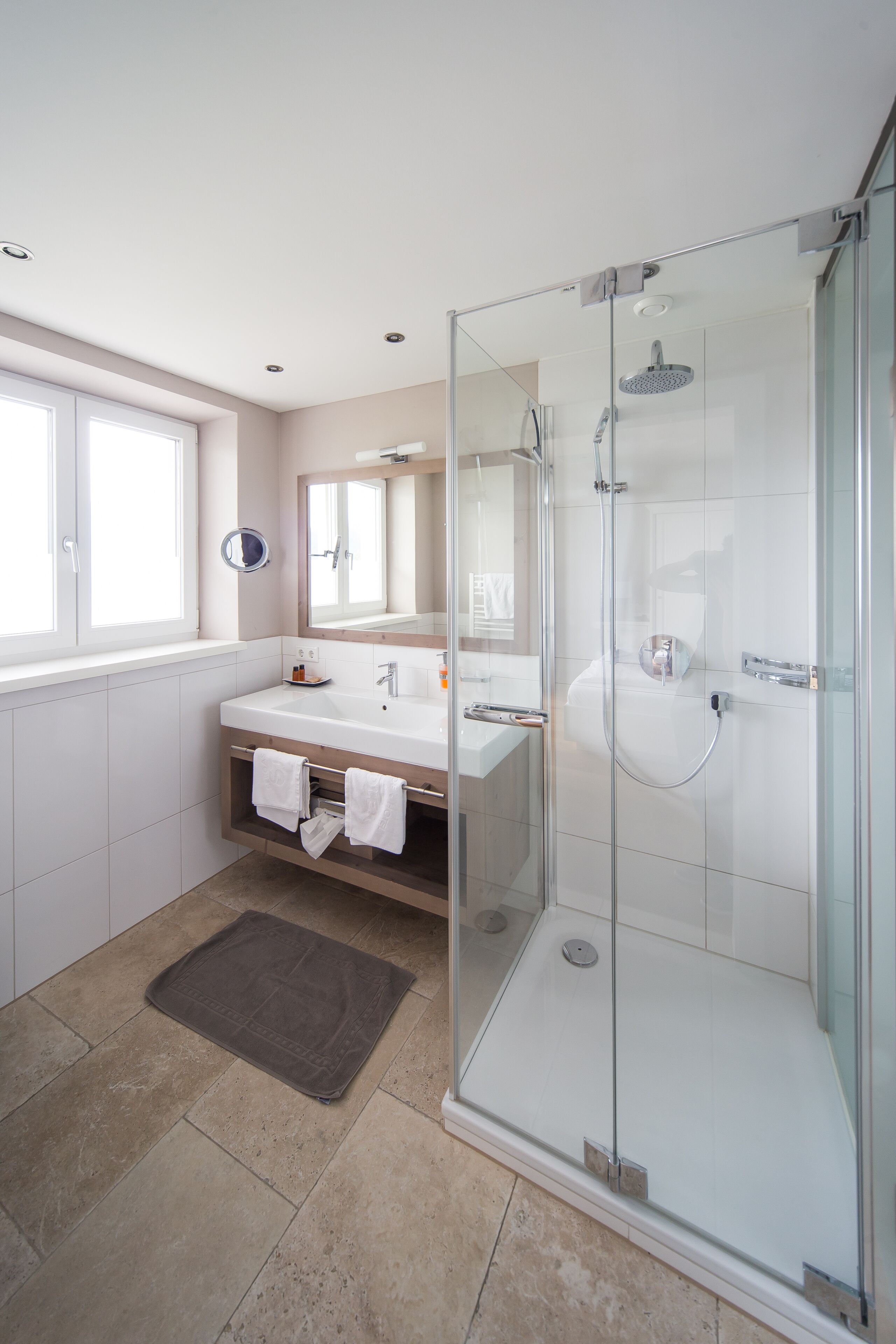 A modern bathroom with a glass-enclosed shower, a vanity with a mirror, and a window providing natural light.