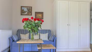 Une pièce avec un canapé bleu, une petite table en bois sur laquelle est posé un vase de roses rouges, et une armoire blanche.