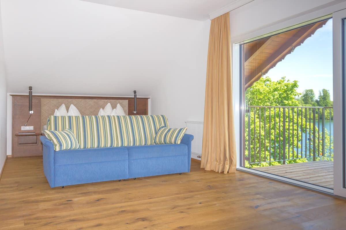Une pièce avec un canapé bleu, un radiateur et une grande porte-fenêtre coulissante donnant sur un balcon avec vue sur la verdure.