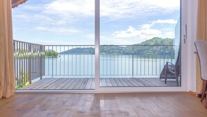 A room with a large sliding glass door leading to a balcony with a view of a lake and hills. - Hotel Stadler am Attersee (Unterach am Attersee)