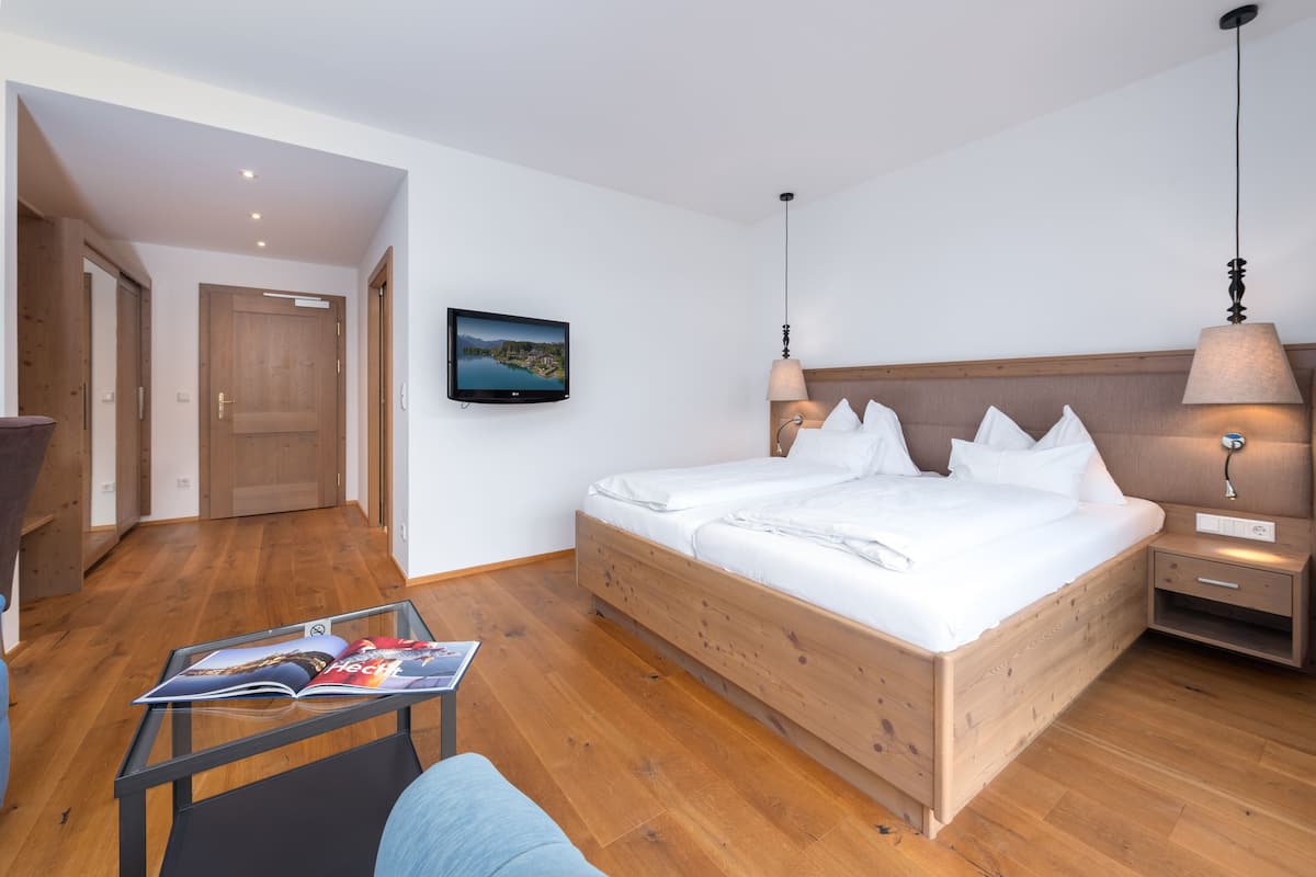 Une chambre à coucher avec un lit en bois, un téléviseur fixé au mur et une table de chevet avec une lampe.