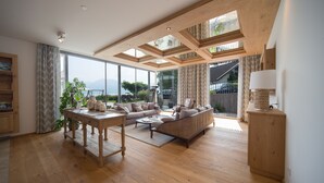 A spacious living room with a wooden ceiling, large windows, a sofa, a coffee table, and a side table. - Hotel Stadler am Attersee (Unterach am Attersee)