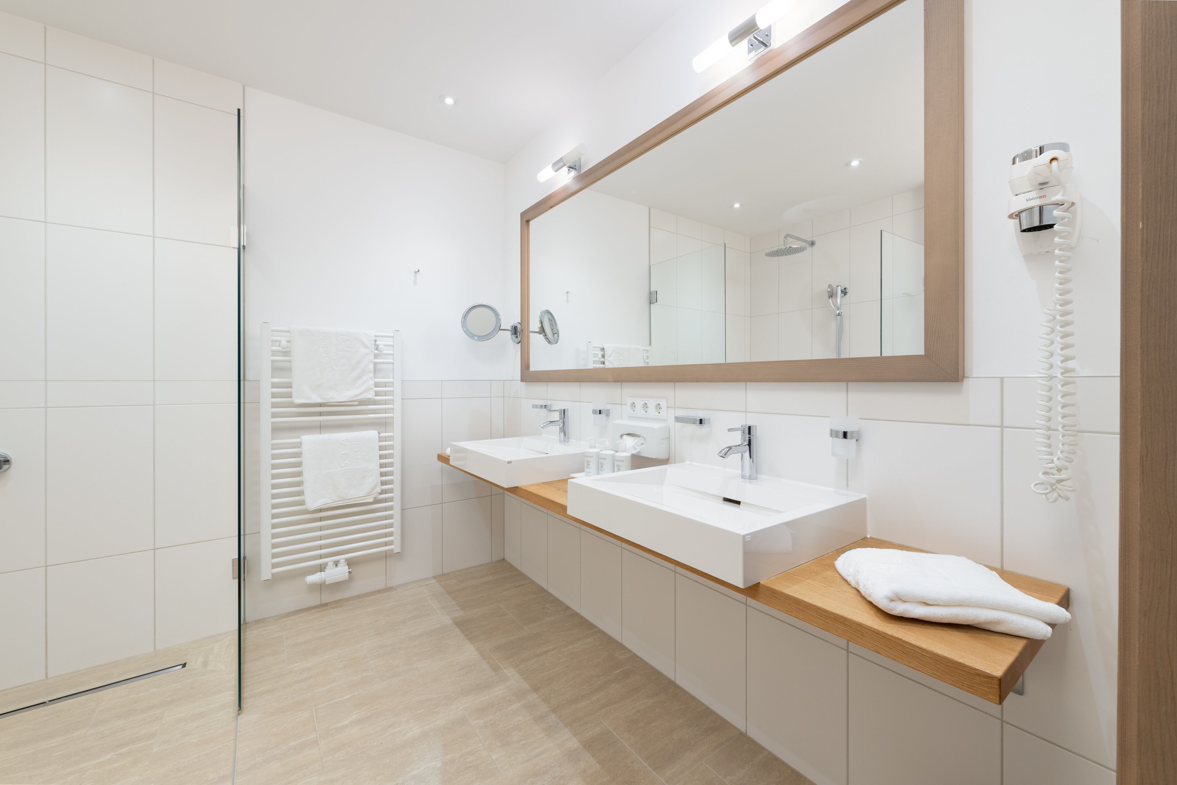 A modern bathroom with two sinks, a large mirror, and a towel rack.