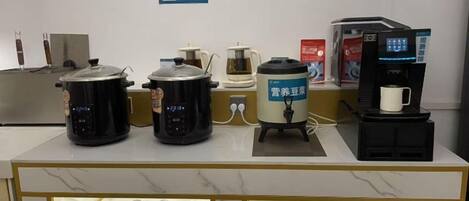 Una zona de cocina con diversos electrodomésticos, incluyendo una cafetera, una cocedora de arroz y una olla de cocción lenta.
