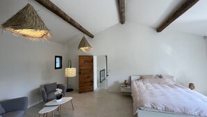 A modern bedroom with a large bed, a gray sofa, a small table with a vase, and a wooden door. - Mas Arietis  (Saint-Rémy-de-Provence)