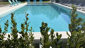 A rectangular swimming pool with clear blue water, surrounded by green plants in the foreground. There are blue Adirondack chairs and lounge chairs along the pool's edge. - Mas Arietis  (Saint-Rémy-de-Provence)