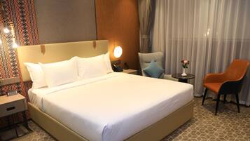 Une chambre d’hôtel avec un grand lit, une table de chevet avec une lampe, une chaise et une petite table sur laquelle est posé un vase.