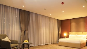 Une chambre d’hôtel avec un lit, une chaise, une petite table avec des fruits et une grande fenêtre avec des rideaux.