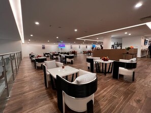Un restaurant moderne doté de plusieurs espaces de restauration, notamment des tables rondes et des banquettes, ainsi qu’un bar.