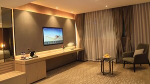 Une chambre d’hôtel moderne dotée d’un grand téléviseur à écran plat fixé au mur, d’un bureau en bois avec une machine à café, d’un vase avec des fleurs, d’une chaise et d’un tapis à motifs.