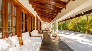 A covered outdoor seating area with a wooden ceiling, white cushioned sofas, and a view of tropical greenery. - Beautiful Villa with Pool Gym and Maid (Punta Cana)