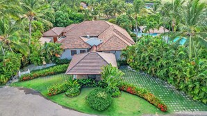 A house with a tiled roof surrounded by lush greenery and palm trees. - Beautiful Villa with Pool Gym and Maid (Punta Cana)