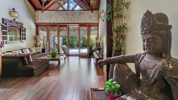 A spacious living room with a large statue, wooden flooring, and a view through glass doors to the outside. - Beautiful Villa with Pool Gym and Maid (Punta Cana)