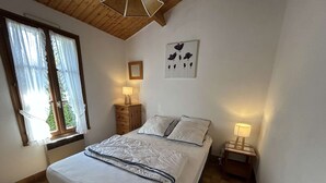 A bedroom with a bed, two bedside tables with lamps, a window with curtains, and a wall with a framed picture. - Cozy 2-BR House Near Beach with Garden, BBQ, and Terraces - Sleeps 4 (Noirmoutier-en-l'Île)