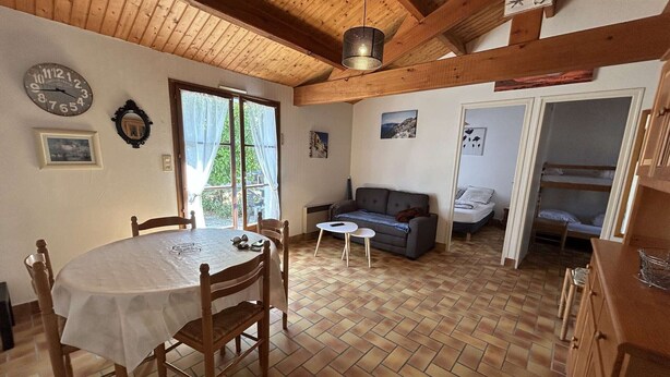 A cozy room with a wooden ceiling, a dining table with chairs, a sofa, and a bunk bed. - Cozy 2-BR House Near Beach with Garden, BBQ, and Terraces - Sleeps 4 (Noirmoutier-en-l'Île)