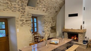 Ein rustikaler Innenraum mit einer Steinwand, einem Kamin, einem langen Holztisch und einer Bank.