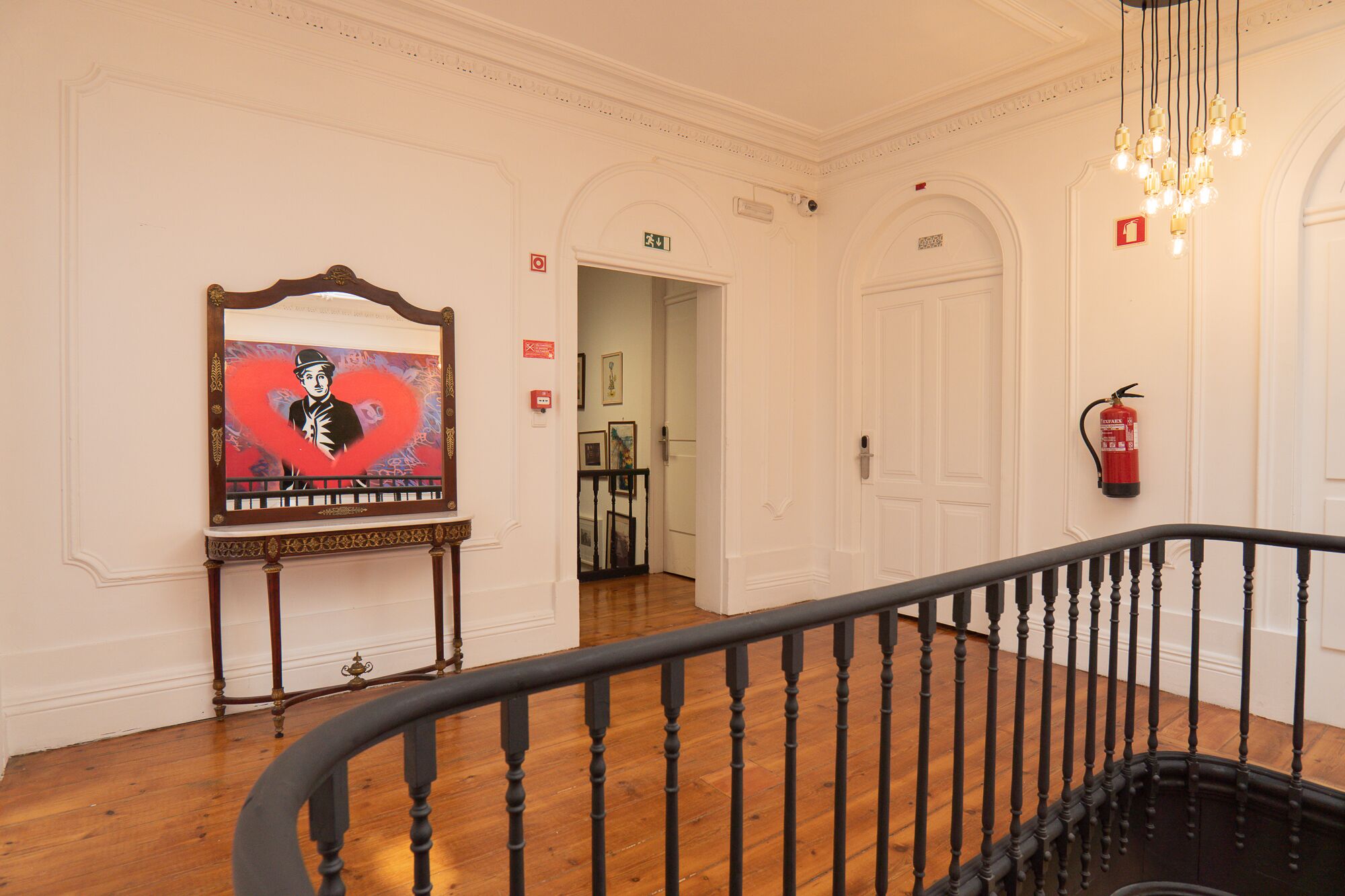 A hallway with a wooden floor, a black railing, and a painting on the wall.