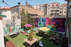 An outdoor patio with artificial grass, seating, and a mural. - Rosalma Hostel (Porto)