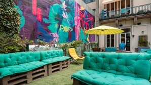 A vibrant outdoor seating area with teal cushioned benches and a yellow umbrella, set against a colorful mural.