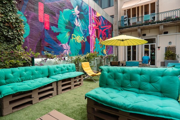 A vibrant outdoor seating area with teal cushioned benches and a yellow umbrella, set against a colorful mural. - Rosalma Hostel (Porto)