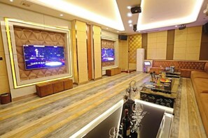 A modern hotel lobby with a wooden floor, two large flat-screen TVs mounted on the walls, a leather sofa, and a coffee table with various items. - Jin Cheng Hotel (Gangu)