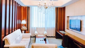 A hotel room with a sofa, armchairs, a coffee table, a TV, and a chandelier. - Jin Cheng Hotel (Gangu)