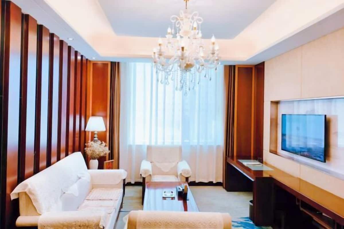 A hotel room with a sofa, armchairs, a coffee table, a TV, and a chandelier.