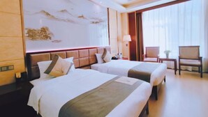 A hotel room with two beds, a large wall mural, a desk with a chair, and a window with curtains. - Jin Cheng Hotel (Gangu)