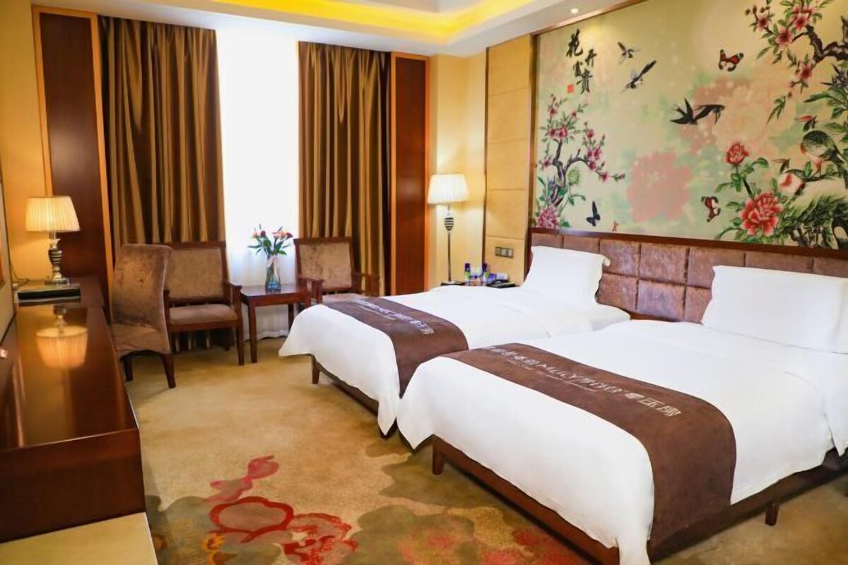 A hotel room with two beds, a desk, chairs, a lamp, and a floral wall mural.