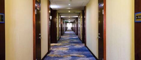 Un pasillo de hotel con alfombra azul, puertas de madera y un cartel que indica el número de habitación 84.